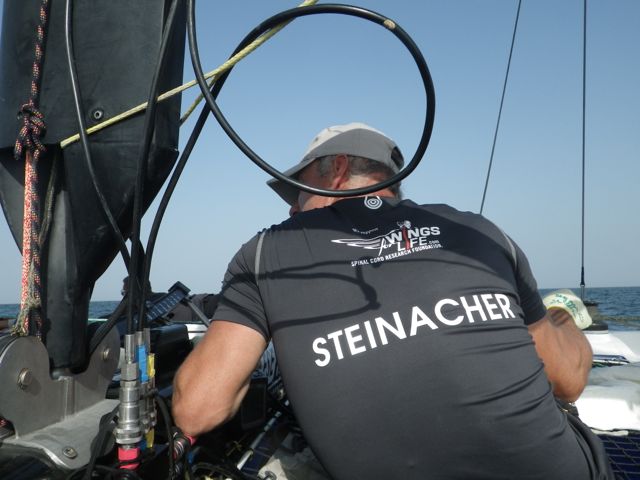 ...Hans Peter Steinacher versteckt sich hinter dem Mast und sieht zu, dass er nicht mit dem Hals in den Hydraulik-Schlauch gerät. Dabei trimmt er... © SegelReporter.com