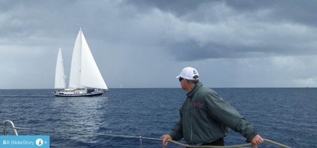 Eine Ketsch zieht noch hübsch Richtung Luvtonne vorbei. Aussie Tim bedient die Gennakerschot. Kurz danach haut der Wind aus der dunklen Wolken den Spi aus den Lieken. © SegelReporter.com